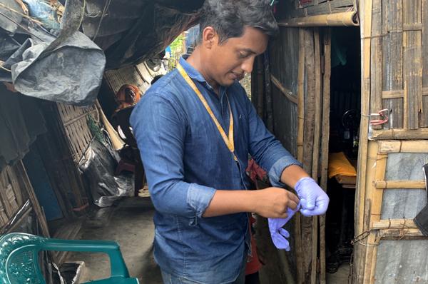 A field technician puts on gloves before administering a vaccine hesitancy survey to a family in the Leda Refugee Settlement.