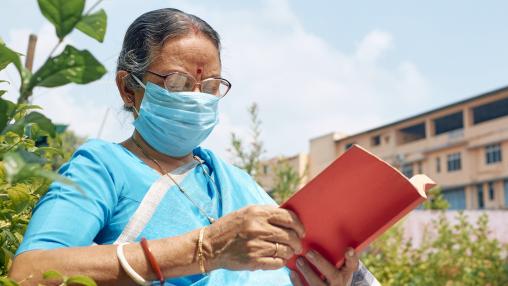 A women in India sits and reads a book while wearing a mask